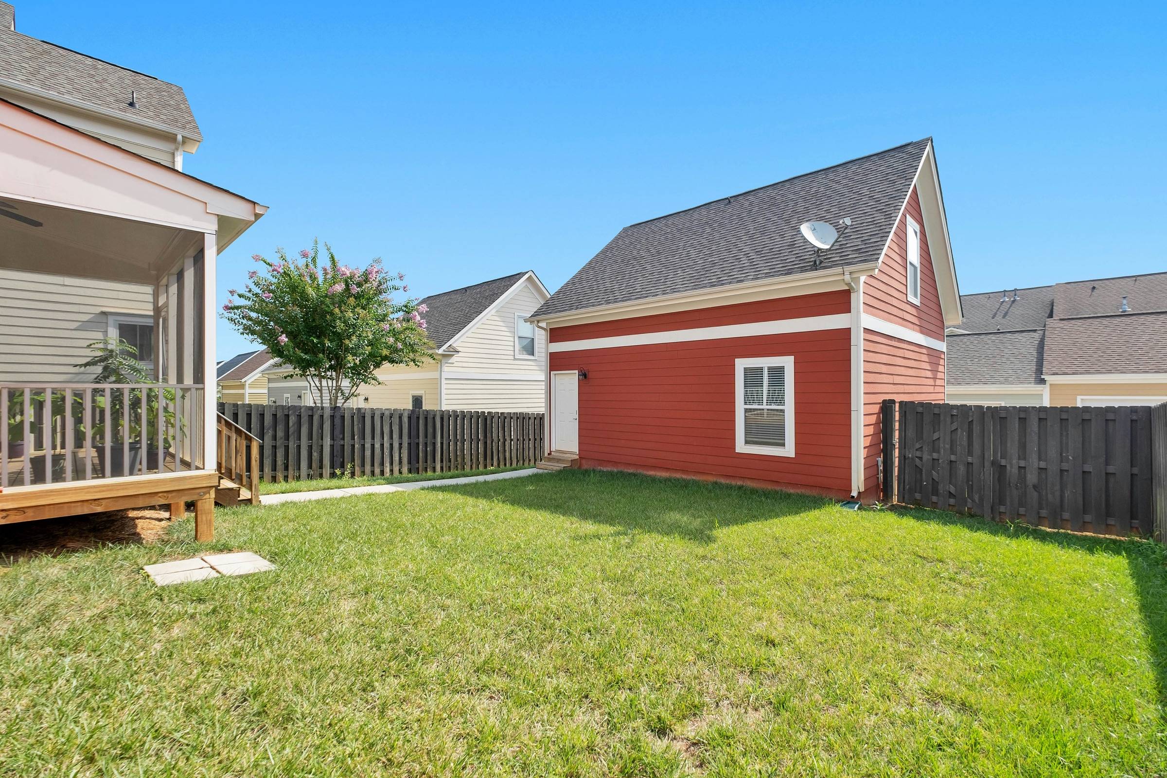 Detached red-sided backyard building with a gabled roof in a fenced, grassy back yard behind a house